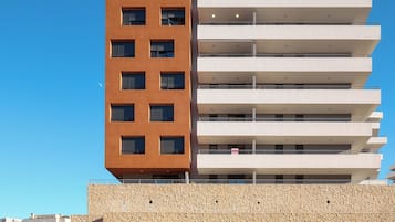 Um edifício moderno de vários andares com fachadas em tons de marrom e branco, entrada de estacionamento e céu azul claro.