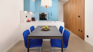 Una cocina moderna con armarios azules, una isla central con un cuenco de fruta, y un comedor con sillas azules.