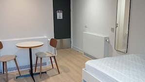 A hotel room with a bed, a round table with chairs, a mirror, and a door. - Student Only The Keel Houses (Edinburgh)