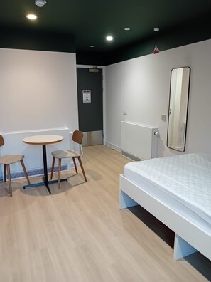 A hotel room with a bed, a round table with chairs, a mirror, and a door. - Student Only The Keel Houses (Edinburgh)