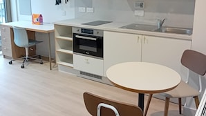A modern kitchen with a built-in oven, a sink, and a dining area with a round table and two chairs. - Student Only The Keel Houses (Edinburgh)