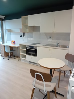A modern kitchen with a built-in oven, a sink, and a dining area with a round table and two chairs. - Student Only The Keel Houses (Edinburgh)