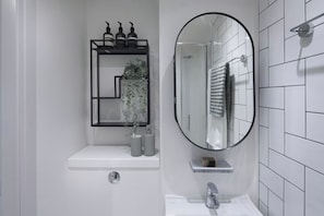 A modern bathroom with a white sink, a mirror, and a shelf with toiletries. - Student Only The Keel Houses (Edinburgh)