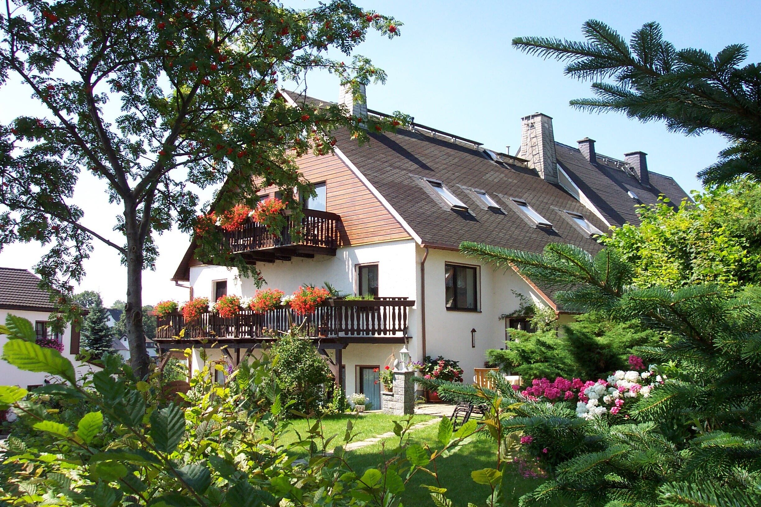 Une maison à deux étages avec un toit en pente, un balcon agrémenté de jardinières et un jardin bien entretenu.