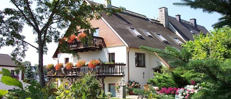 Une maison à deux étages avec un toit en pente, un balcon agrémenté de jardinières et un jardin bien entretenu.