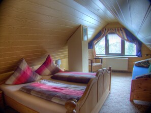 A bedroom with a sloped ceiling, a bed with multiple pillows, a chair, a table with a lamp, and a window with curtains. - Apartment 'FeWo Pyramide' with Shared Garden and Wi-Fi (Marienberg)