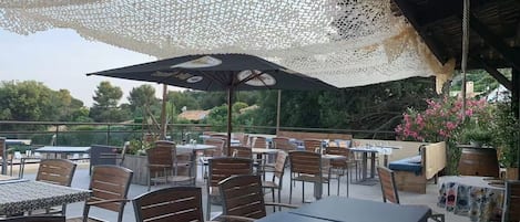 Une terrasse extérieure avec des tables et des chaises, un auvent décoratif et une vue sur le paysage environnant.