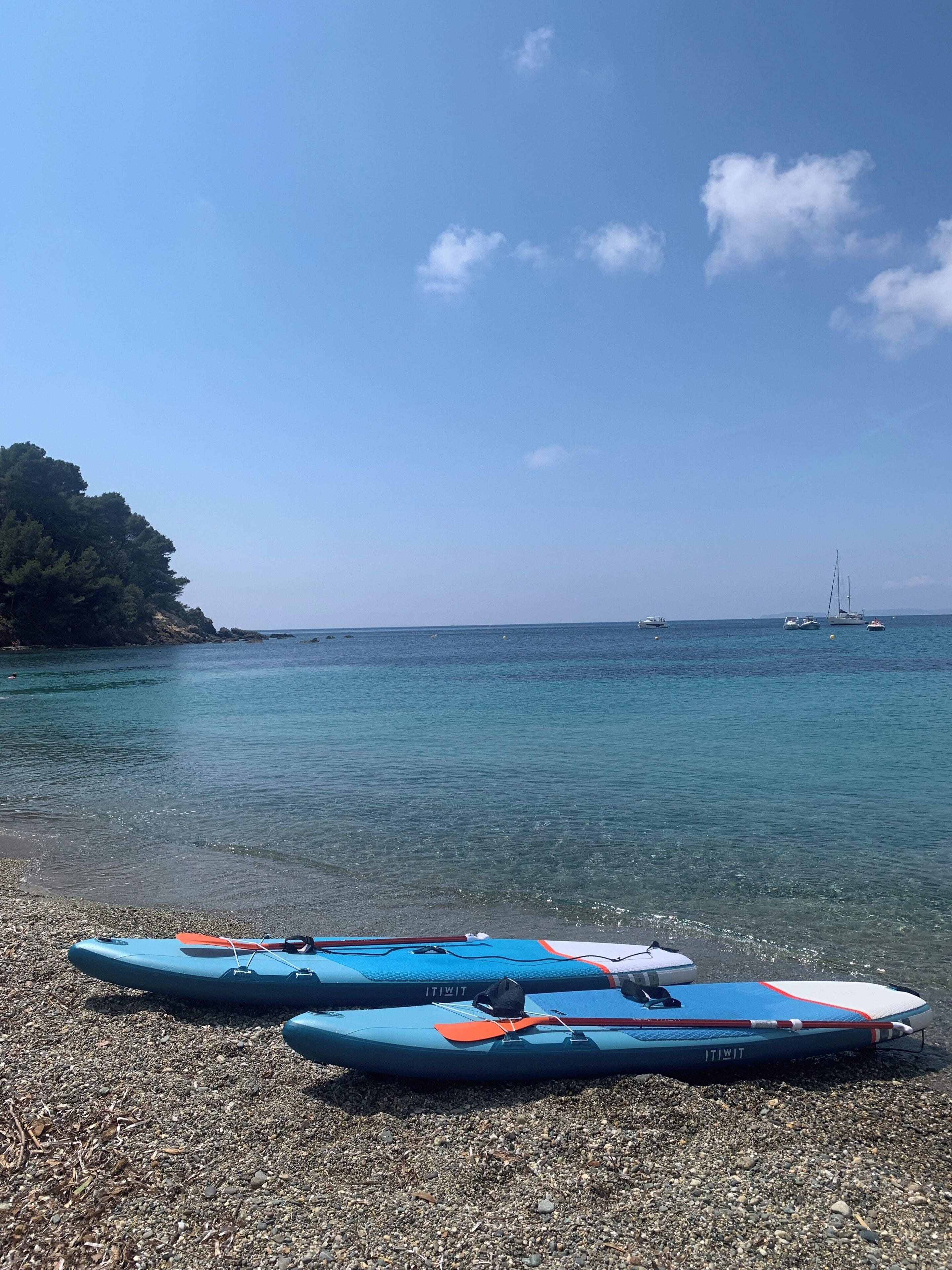 Une plage de galets avec deux kayaks bleus et un voilier à l’horizon.