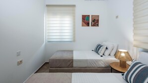 A small, neatly arranged bedroom with a bed, a bedside table with a lamp, and a window with blinds. - Marilianas Apartment (Platanias)