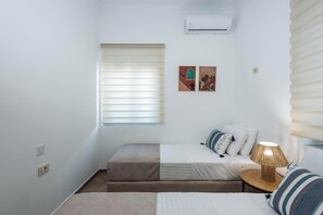 A small, neatly arranged bedroom with a bed, a bedside table with a lamp, and a window with blinds. - Marilianas Apartment (Platanias)