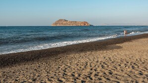 A beach with a rocky outcrop in the distance, a pebbly shore, and a clear sky. - Marilianas Apartment (Platanias)