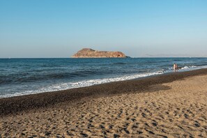 A beach with a rocky outcrop in the distance, a pebbly shore, and a clear sky. - Marilianas Apartment (Platanias)