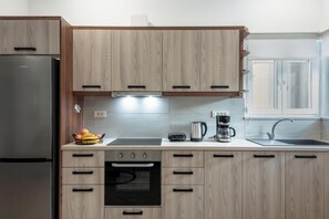 A modern kitchen with wooden cabinets, a built-in oven, a coffee maker, and a fruit bowl. - Marilianas Apartment (Platanias)