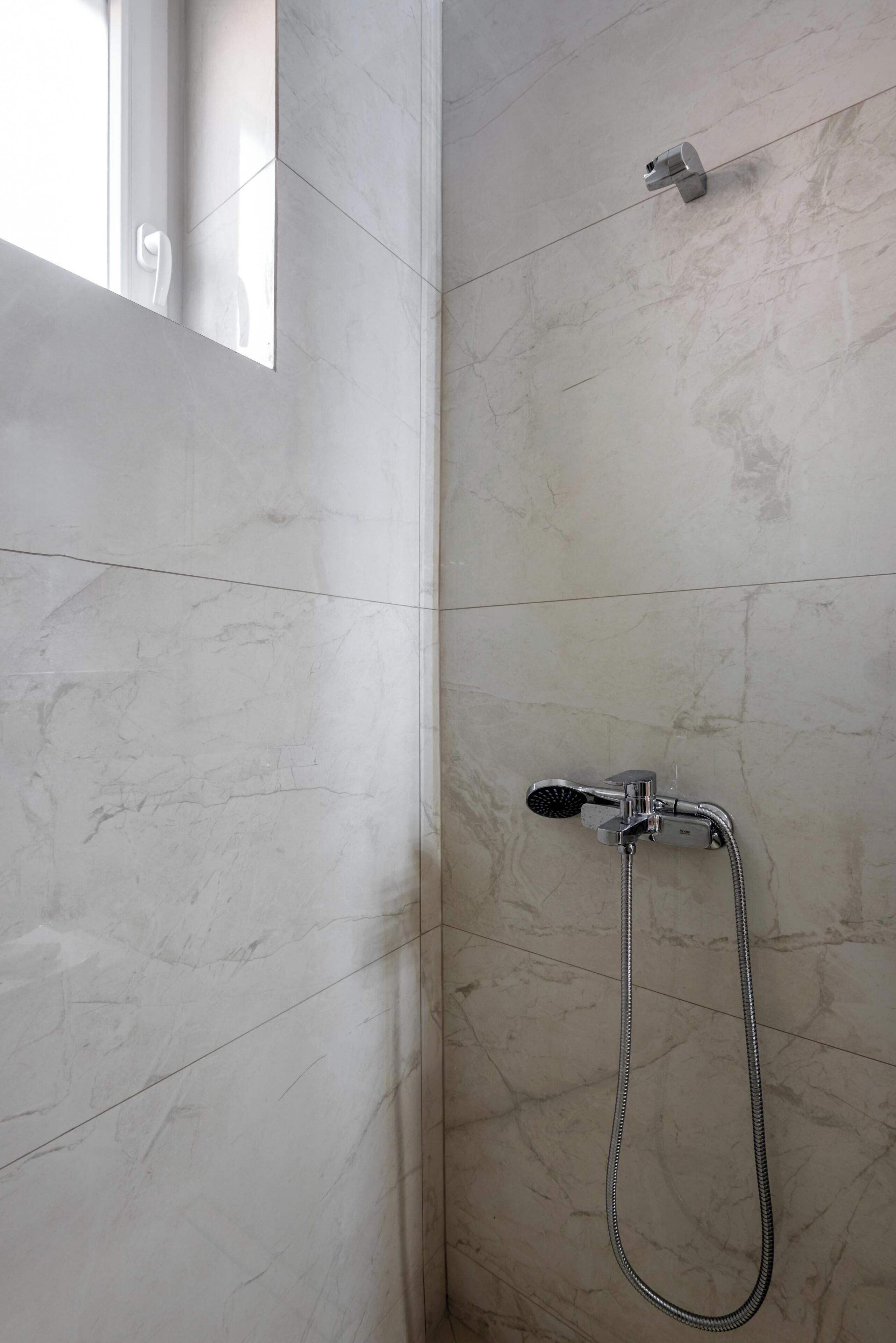 A shower with a handheld showerhead and a wall-mounted faucet.