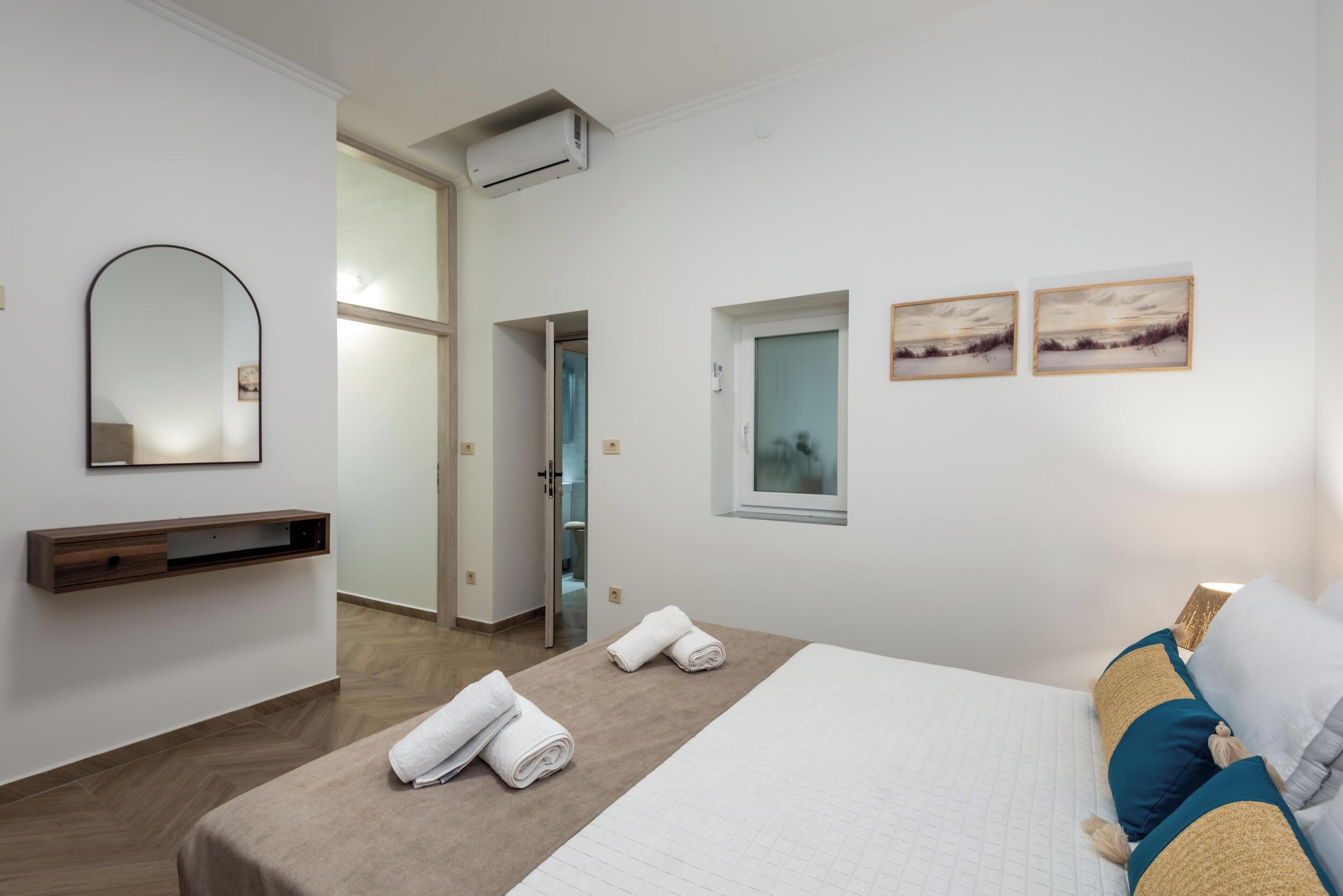 A hotel room with a bed, a bedside table, a mirror, a window, and artwork on the wall.