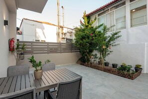 Een terras buiten, met een tafel en stoelen, omringd door potplanten en een metalen hek.