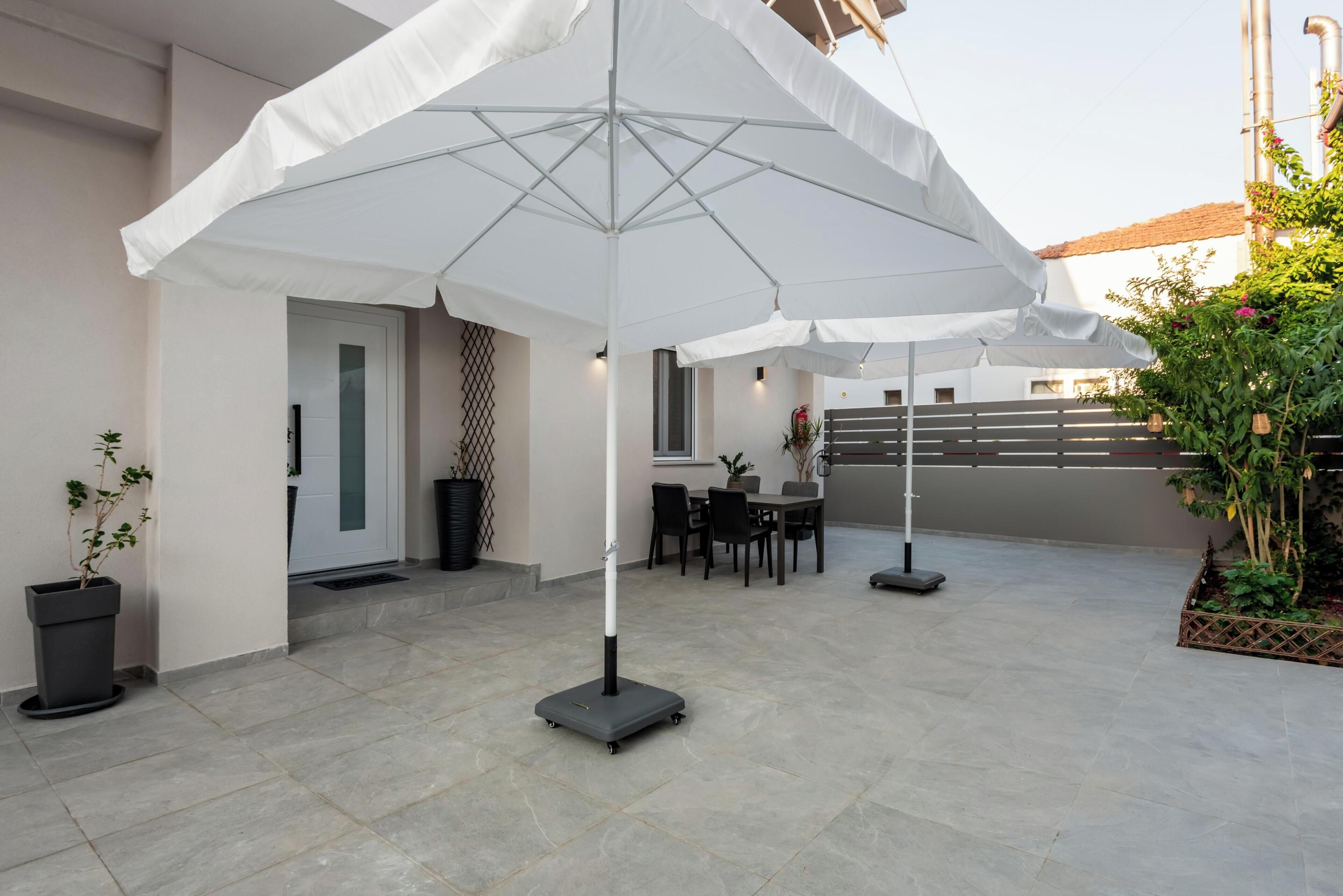A patio area with a table and chairs, a white umbrella, and potted plants.