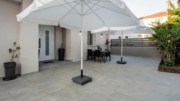 A patio area with a table and chairs, a white umbrella, and potted plants. - Marilianas Apartment (Platanias)
