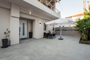 A modern outdoor patio with a dining table and chairs, a white umbrella, and potted plants. - Marilianas Apartment (Platanias)