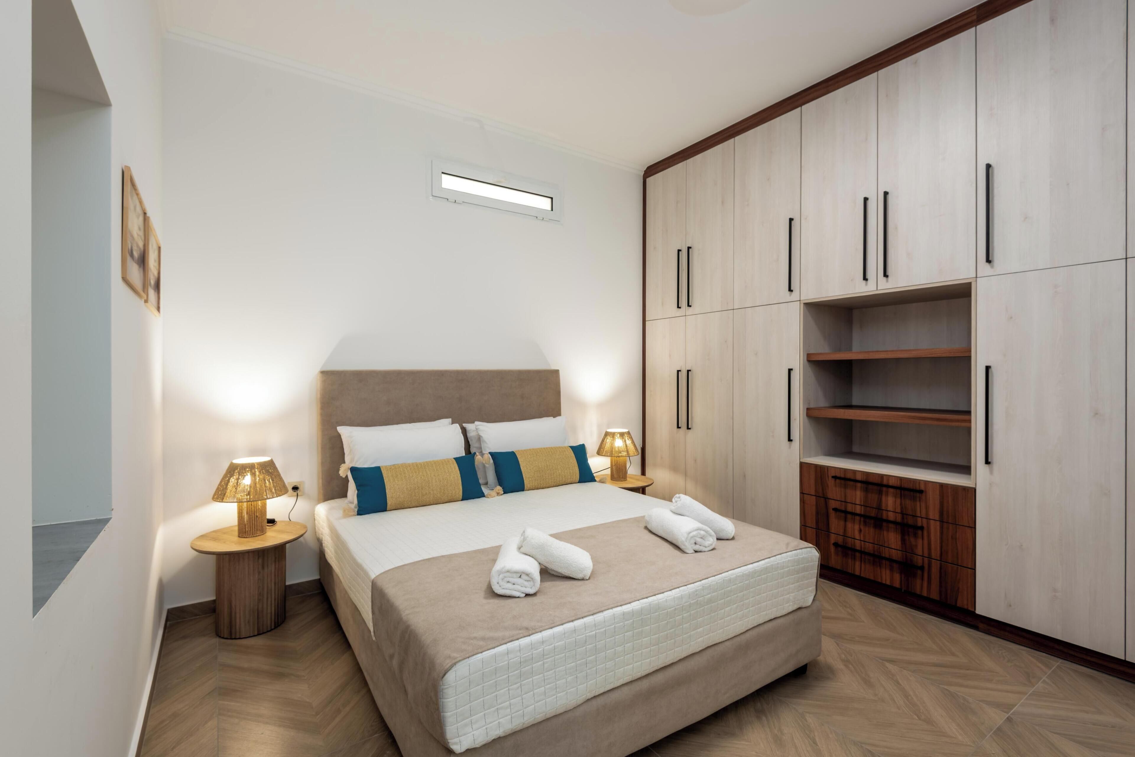 Una habitación de hotel con cama, lámparas de noche, armario y una pequeña mesa.