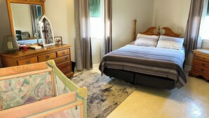 A bedroom with a bed, a dresser, a mirror, and a window with curtains.