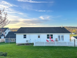 A single-story house with a white exterior, a covered porch with red chairs, and a clear sky.