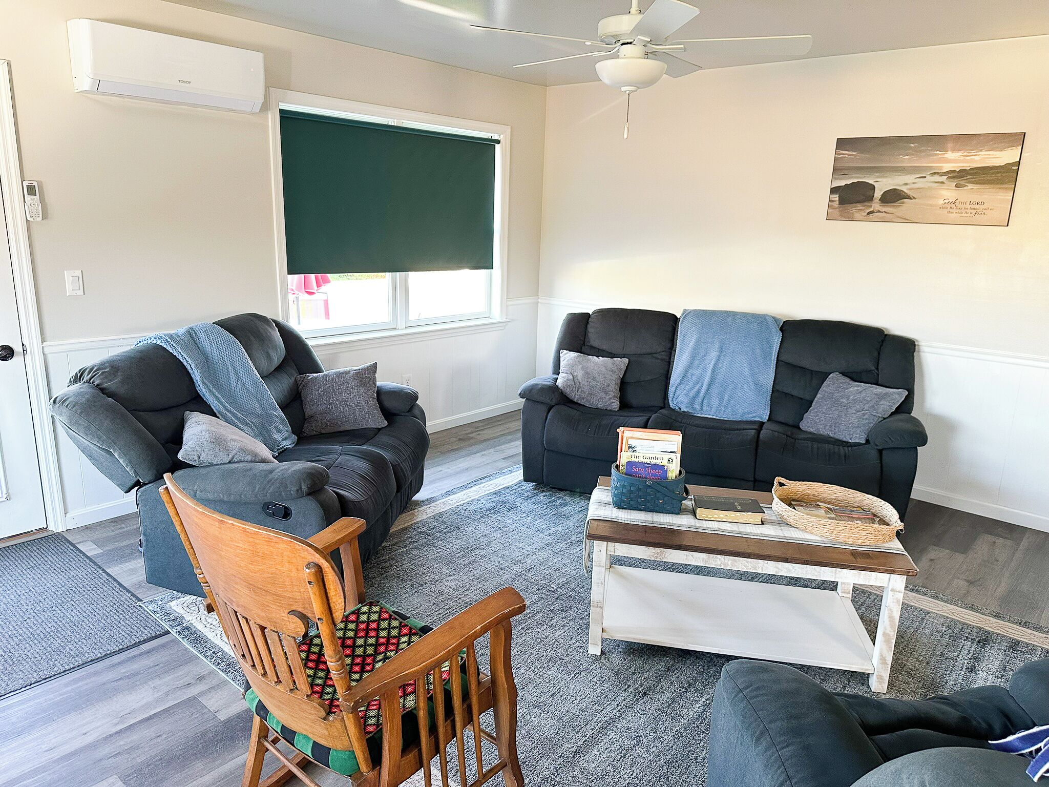 Un salon avec deux canapés, un fauteuil en bois, une table basse avec des livres et un ventilateur de plafond.