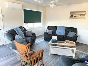 A living room with two sofas, a wooden chair, a coffee table with books, and a ceiling fan.