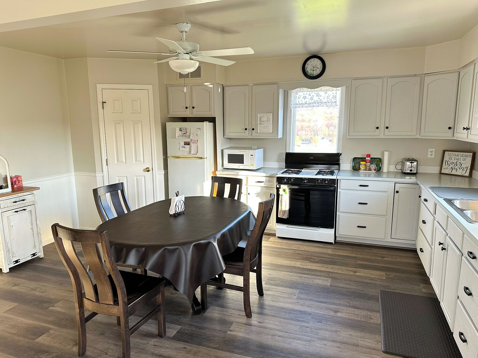 A kitchen with white cabinets, a microwave, stove, and a dining area with a table and chairs.