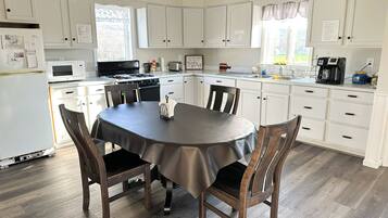 Une cuisine avec des meubles blancs, une cuisinière, un évier et une table à manger avec des chaises.
