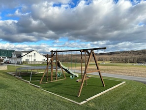 A playground with swings and a trampoline in a grassy area with a building in the background.