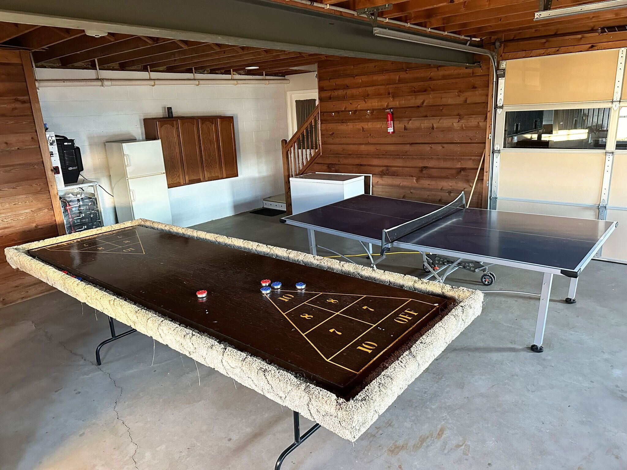 A billiards table with a shuffleboard setup in a room with wooden walls and a concrete floor.