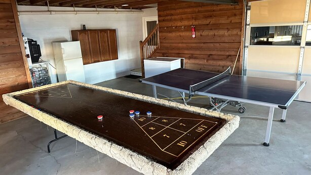 A billiards table with a shuffleboard setup in a room with wooden walls and a concrete floor.
