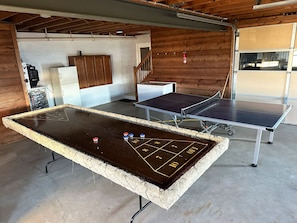A billiards table with a shuffleboard setup in a room with wooden walls and a concrete floor.