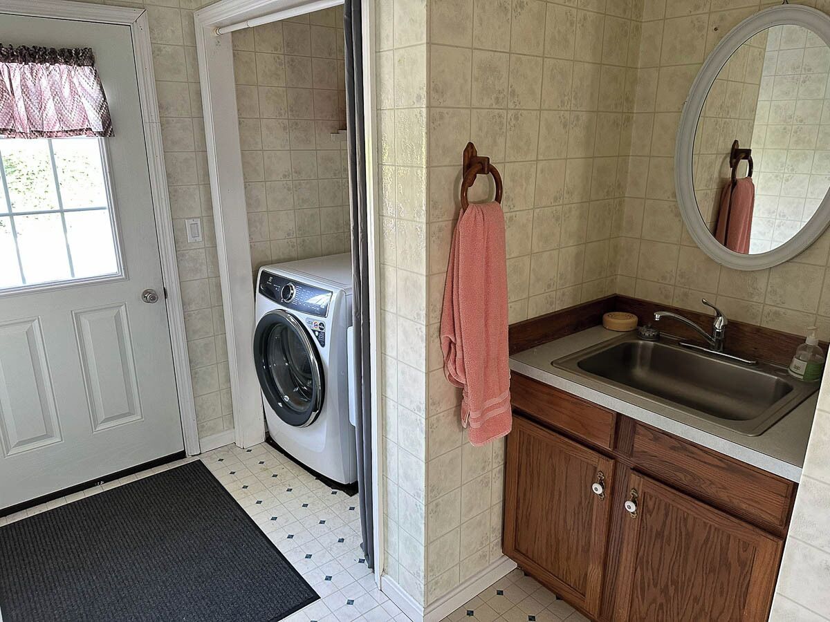 A compact laundry room with a washing machine, a sink, and a mirror.