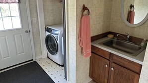 A compact laundry room with a washing machine, a sink, and a mirror.