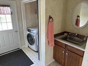A compact laundry room with a washing machine, a sink, and a mirror.