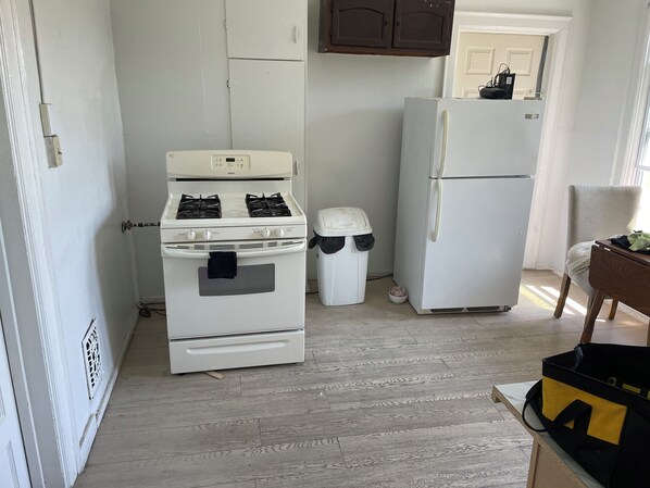 Una cocina con estufa blanca, refrigerador blanco y un bote de basura.
