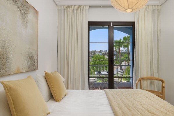 A bedroom with a bed, pillows, a view of a balcony with outdoor furniture, and a painting on the wall. - Elegant 2BR in Los Arqueros Golf & Country Club (Benahavís)