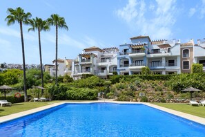 A resort with a swimming pool, multiple-story buildings, and palm trees. - Elegant 2BR in Los Arqueros Golf & Country Club (Benahavís)