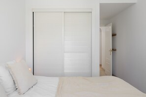A bedroom with a bed, a white closet, and a door leading to another room. - Elegant 2BR in Los Arqueros Golf & Country Club (Benahavís)