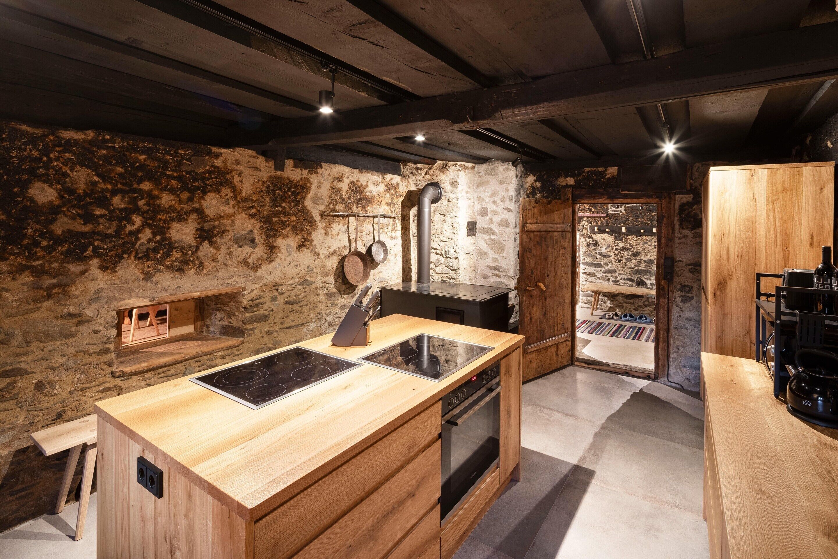Une cuisine rustique avec un plan de travail en bois, un four encastré et un mur en pierre.