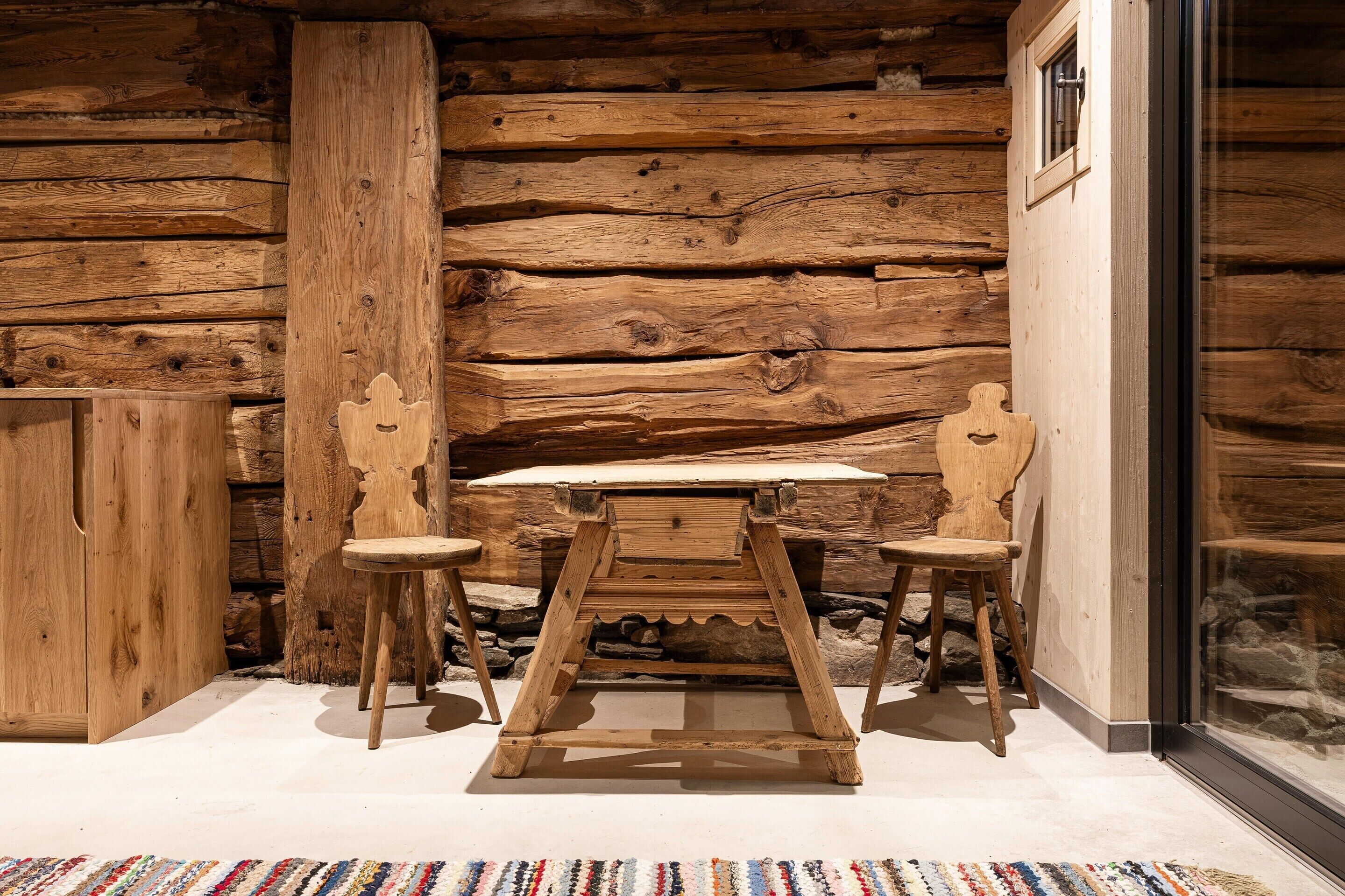 Un intérieur rustique en bois, avec une table et deux chaises, un mur en pierre et une fenêtre.