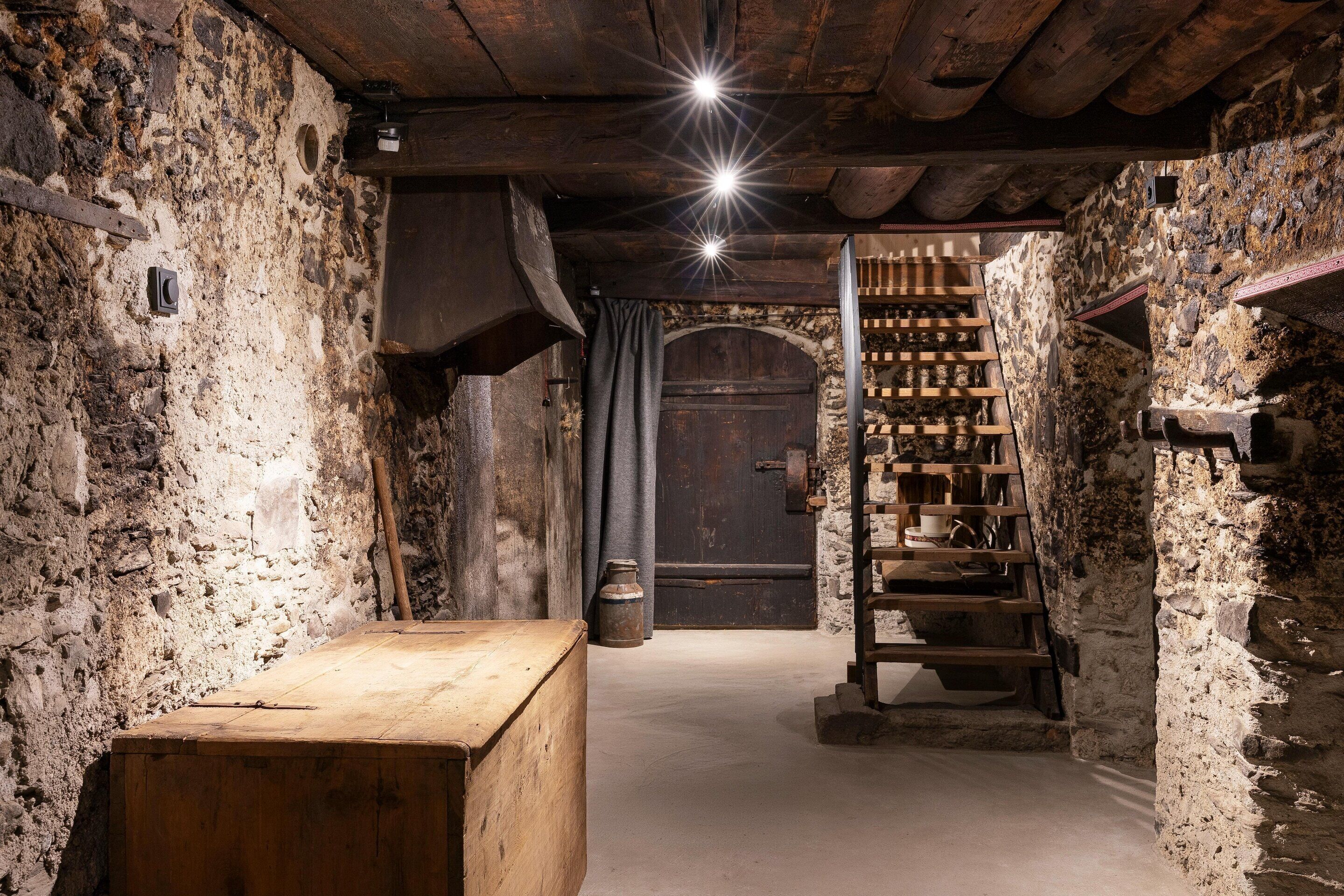 Een rustiek interieur met een houten bank, stenen muren, een houten trap en een donkerhouten deur.
