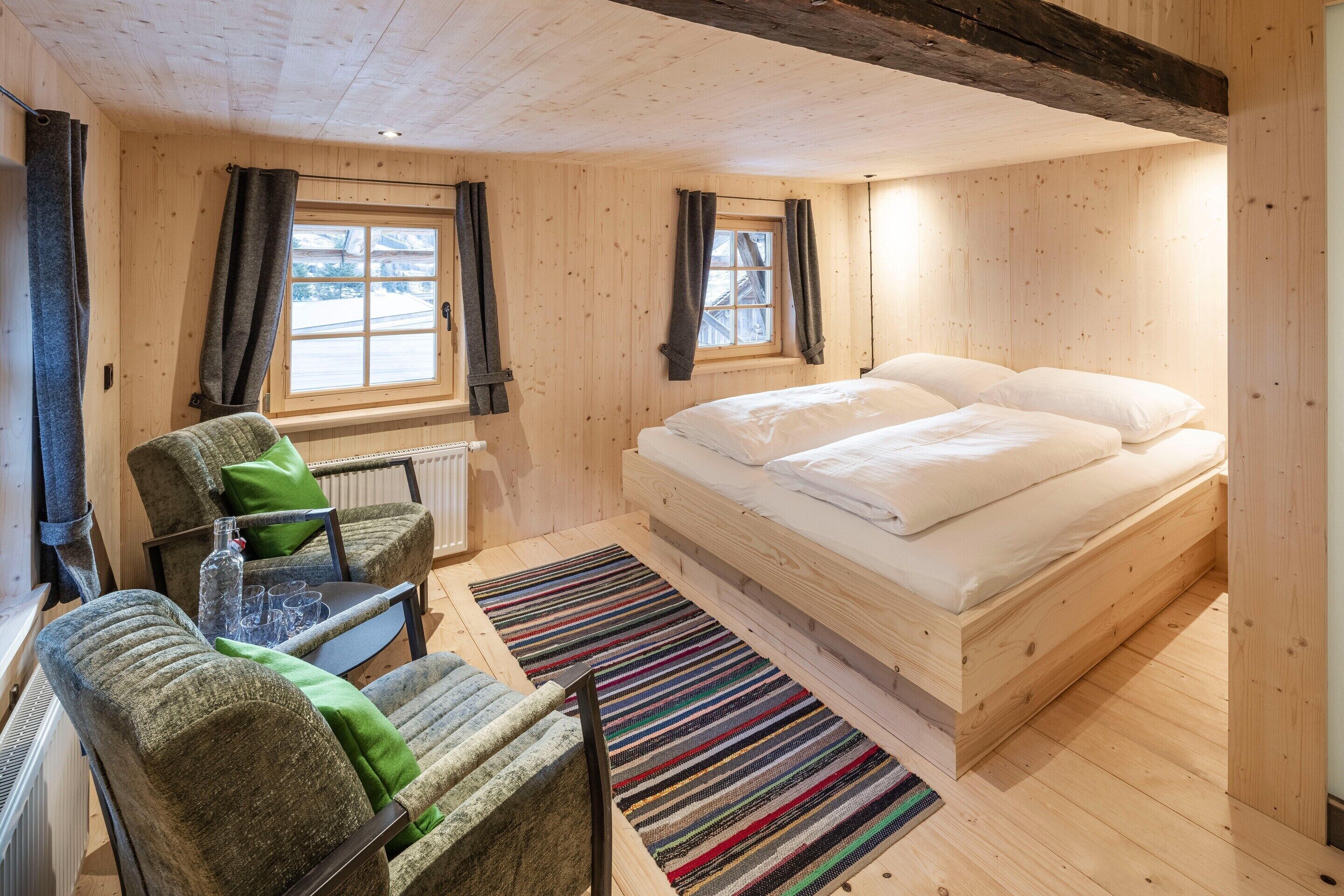 Una habitación con paneles de madera, una cama, una silla, un radiador y una ventana.