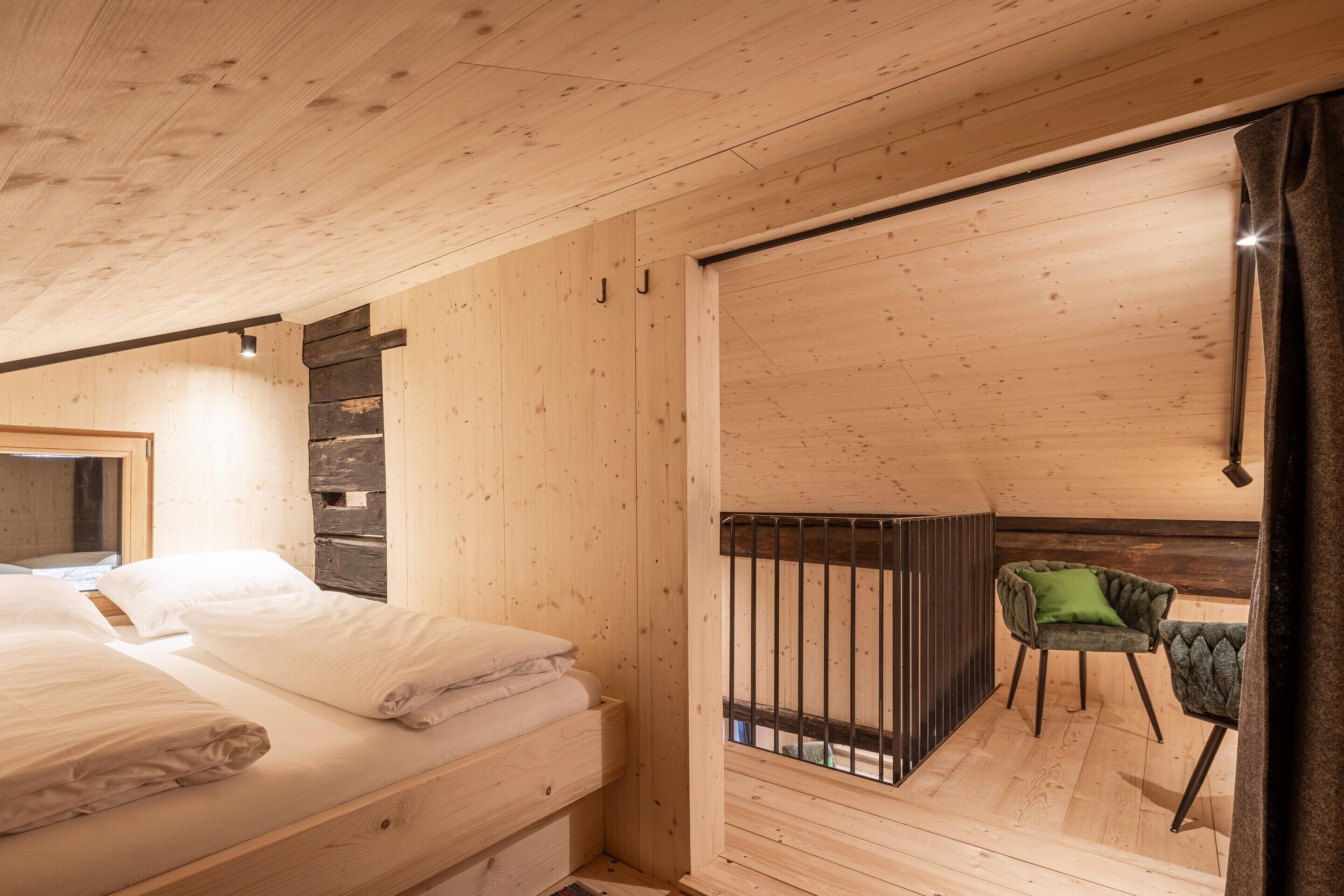 Un intérieur en bois comprenant un lit, une chaise et une porte coulissante donnant sur un espace extérieur.