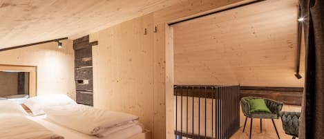 Un interior de madera con una cama, una silla y un acceso corredizo a un espacio exterior.