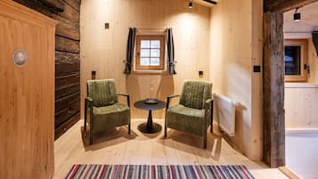 Una habitación acogedora con paredes de madera, una ventana, dos sillas, una mesita y un radiador.