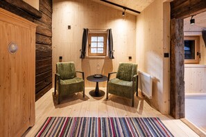 Una habitación acogedora con paredes de madera, una ventana, dos sillas, una mesita y un radiador.