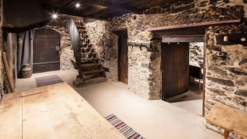 Interior rústico de piedra con una mesa de madera, una escalera y una chimenea.